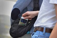 Person placing a smartphone into a black waist bag at an outdoor setting.