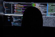 Person analyzing code on multiple screens for cybersecurity threats.