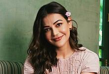 Kajal Aggarwal smiling in a pink outfit with floral accessories in her hair.
