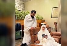 Sana Khan sitting on a brown leather chair, reading a book, with a man standing beside her in a waiting l.