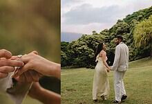 Couple getting engaged outdoors with lush green trees and cloudy sky in the background.