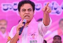 KTR speaking passionately at a public event with a pink backdrop and supporters.