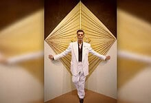 Celebrity posing in white suit against geometric background for Koffee With Karan season 9.