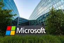Microsoft logo outside a modern office building in Hyderabad, India, with greenery around.