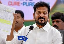 Revanth holding a document during a public event, speaking into a microphone.