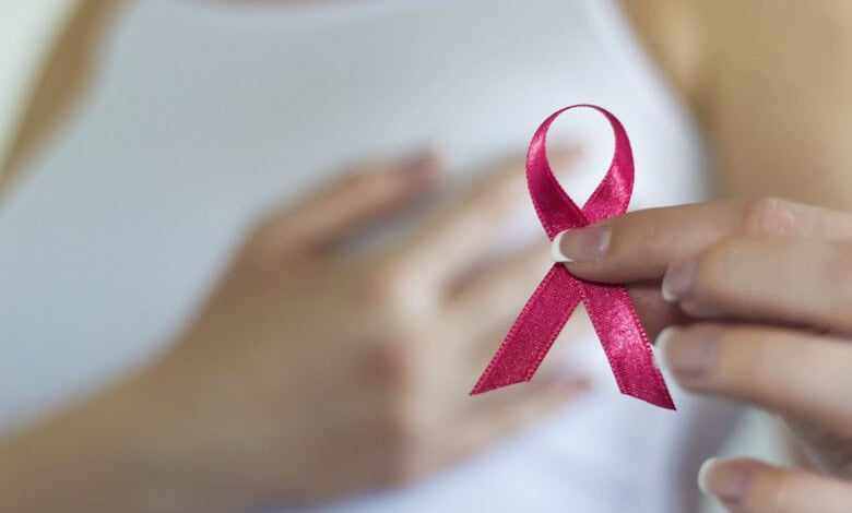 Person holding pink ribbon symbol for breast cancer awareness close to chest.