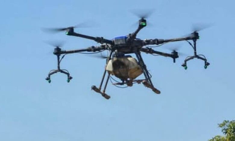 Unmanned drone flying in clear blue sky with visible propellers and sensors.