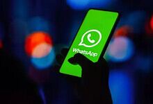 Person holding a smartphone displaying the WhatsApp logo with a dark, blurred background.