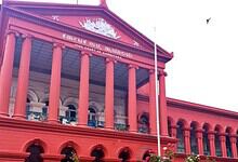 Historic red courthouse building with columns and Kannada script at the top.