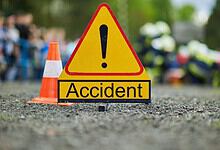 Accident scene with warning sign and blurred emergency responders in background.