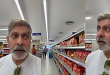 Man with grey hair and beard shopping in a supermarket aisle with snack shelves.