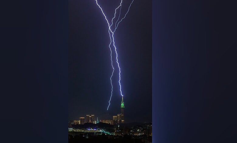 A lightning bolt strikes the illuminated Makkah Clock Tower at night as the city skyline lies below.
