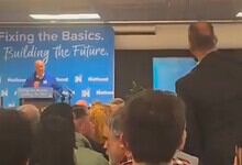Protester confronts NZ PM Luxon during a political event with a crowd present.