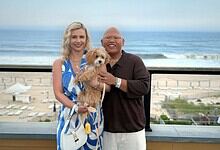 Happy couple with a dog on a balcony overlooking the beach in en_GB.