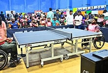 Wheelchair user playing table tennis at a busy indoor sports event in Hyderabad.