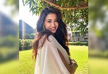 Disha Patani smiling outdoors in a beige outfit with greenery in the background.