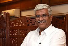Shekhawat smiling in a formal setting, wearing a white shirt and glasses.