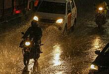 Motorcycles and cars navigating flooded streets during heavy monsoon rains in Hyderabad.