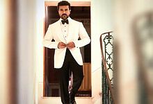Man in white tuxedo with black bow tie standing at doorway, stylish and confident.