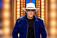 Salman Khan in a blue jacket and white hat on a brightly lit stage.