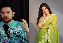 Comedian Samay Raina speaking at an event with a woman in a green saree smiling nearby.