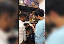 Two men browsing books in a bookstore, one holding a book and the other pointing at it.