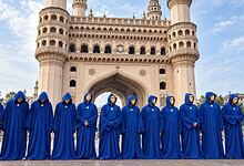 Group of people in blue robes and masks standing in front of Charminar, Hyderabad.