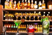 Variety of colourful cocktails on a bar counter with blurred bottles in background.