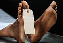 Dead body with a tag attached, lying on a surface in a crime scene or medical setting.