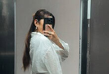 Woman taking a mirror selfie with a smartphone in an elevator.