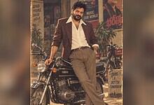 Revanth Reddy in 1980s style outfit with vintage motorcycle in a retro-themed setting.