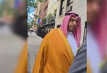 Palestinian American in traditional attire confronts Saudi official outside building.