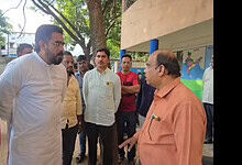 Group of men engaged in conversation outdoors near a tree and building.