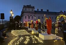 People gathered outdoors during evening with decorative lights and a performer on a stage.