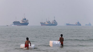 Two children in swimwear playing with white objects in the shallow sea water.