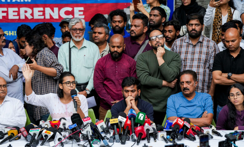 Group of people at a press conference with microphones and cameras in front.