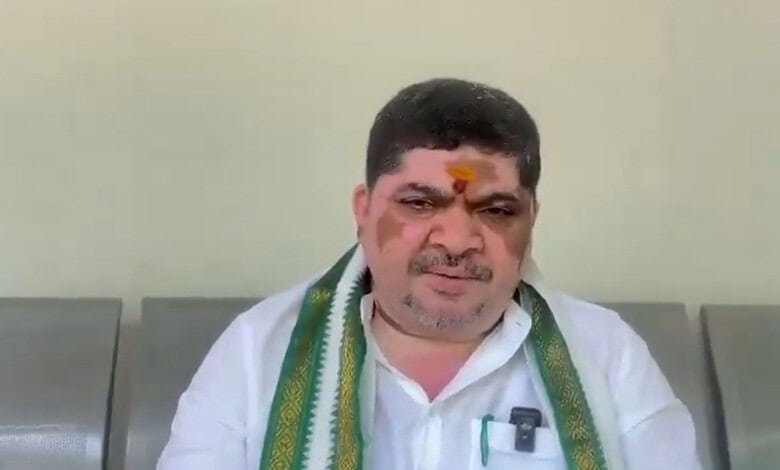 Ponnam Prabhakar wearing a white shirt and a green scarf, sitting indoors with a neutral background.
