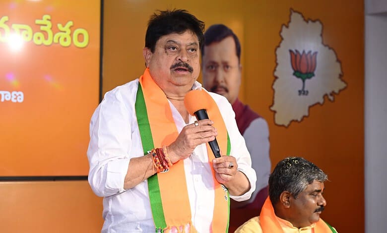 Telangana BJP chief speaking at a political event with party symbols and leaders in the background.