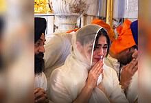 A woman in white traditional attire prays with tears at Golden Temple during her visit.