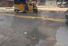 Street scene with auto rickshaw, motorcycles, and cars on a wet road in India.