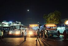 Nighttime scene at a bus station with multiple buses and people under a dark sky.