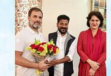 Three people, two men and a woman, smiling with a bouquet of flowers in a room.