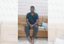 Young man sitting on a brown sofa in a modern room with white hexagonal wall tiles.