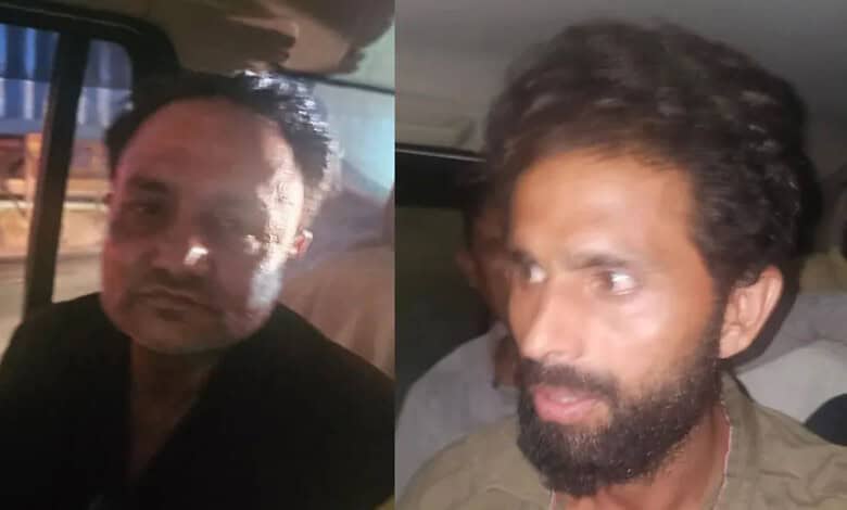 Two men with dark hair and beards in a vehicle, one looking at the camera, the other looking away.