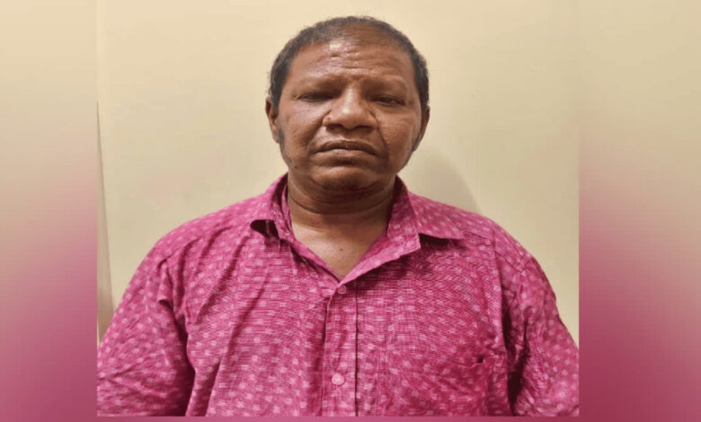 Man in pink shirt with serious expression against plain background.