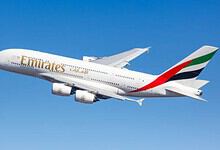 Emirates airplane flying in clear blue sky, showcasing airline branding and design.