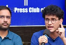 Two men speaking at a press conference, one with glasses and the other with curly hair and glasses.