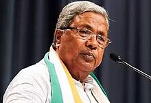 Former CM Siddaramaiah speaking at a press conference with a microphone and a dark background.