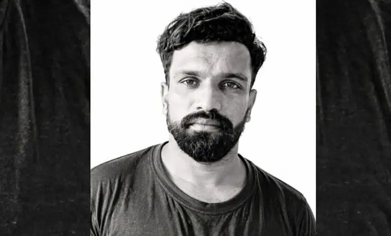 Black and white portrait of a man with a beard and short hair, wearing a dark t-shirt.