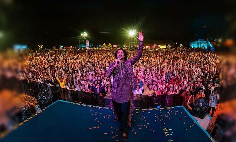 A speaker addresses a large crowd at night during a public event with bright lights and tents in the背景.